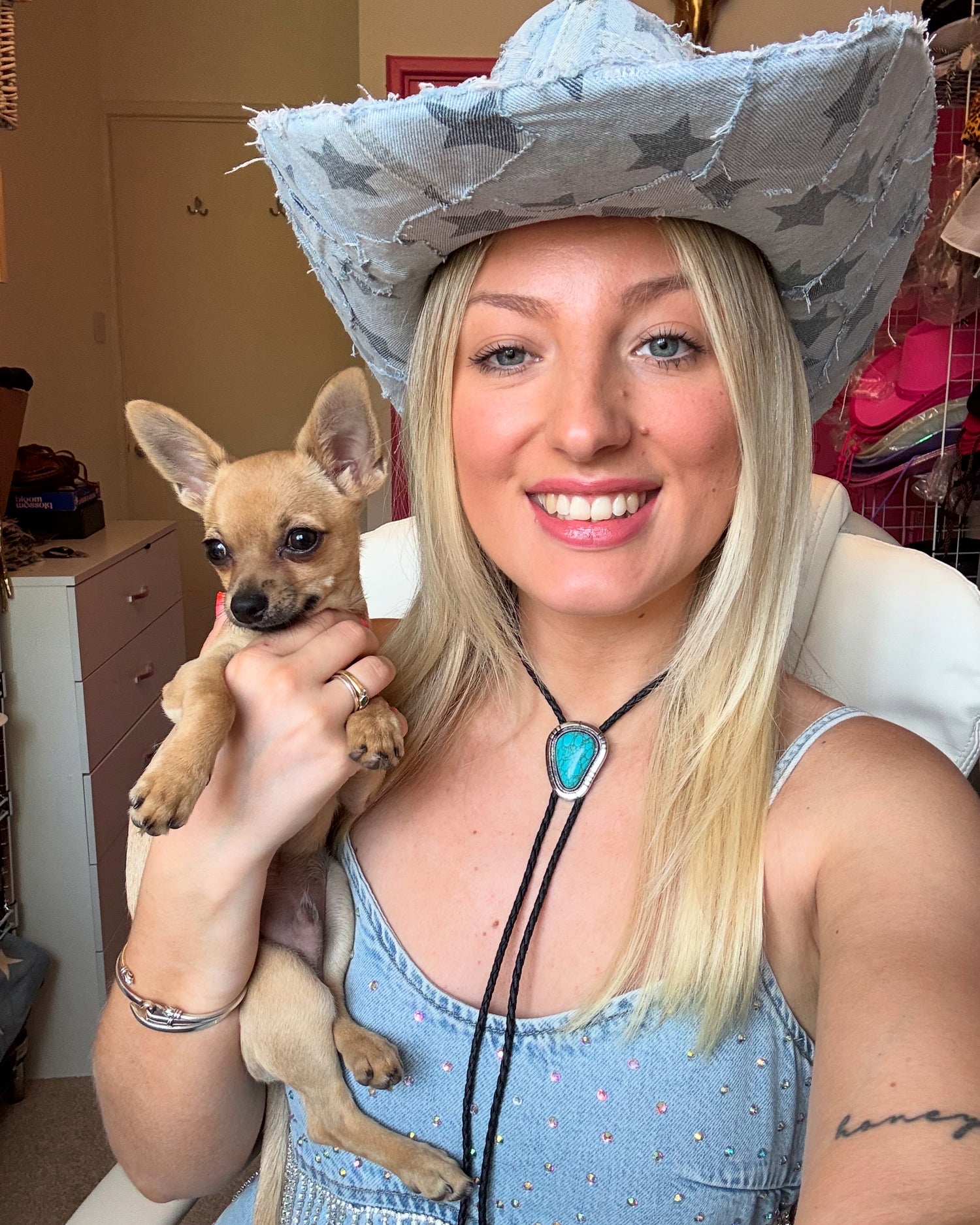 Woman wearing a cowboy hat holding a small dog indoors